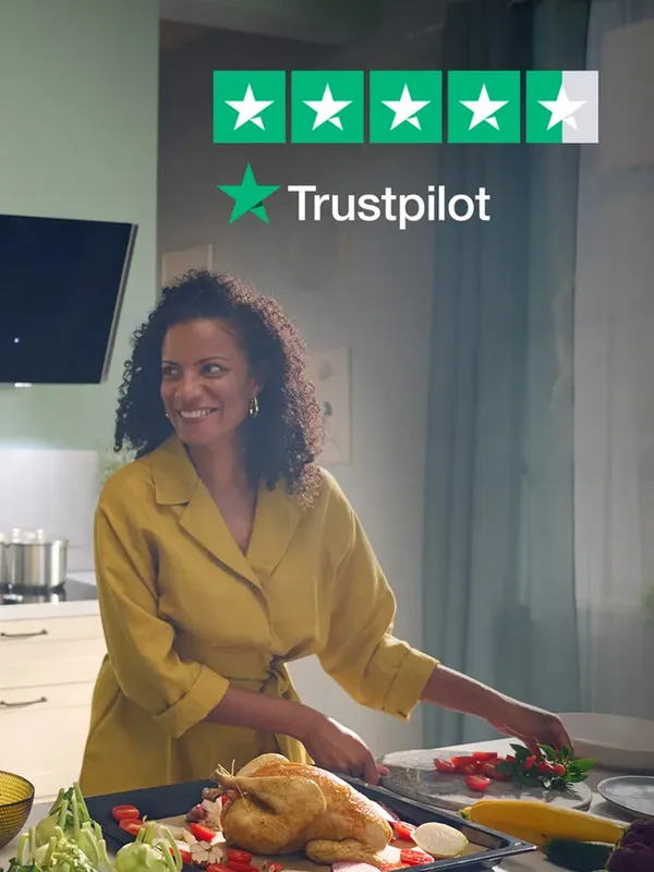 Woman in yellow coat smiling while preparing food in kitchen with Trustpilot rating sign.