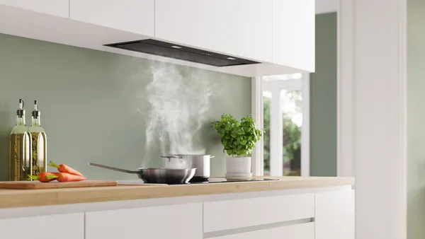 Modern kitchen with white cabinets, wooden countertop, cooking pot emitting steam, and potted plant.