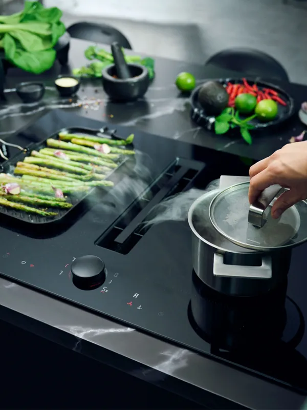 Cooking on a modern stove with fresh vegetables, pans, and cooking utensils.
