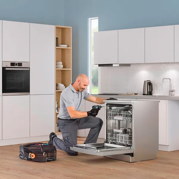 A technician repairs a Bosch dishwasher in a blue kitchen.