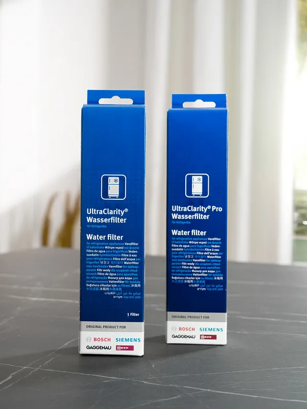 Two blue UltraClarity Pro Wasserfilter water filter boxes on a gray surface with a blurred light curtain background.