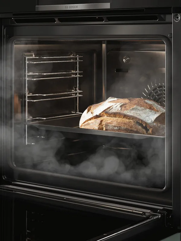 Forno Bosch con funzione AddedSteam e design elegante nero, aperto e con un pane all'interno appena cotto