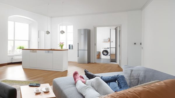 A brightly lit room where a family relaxes on a couch with washing machine in the background