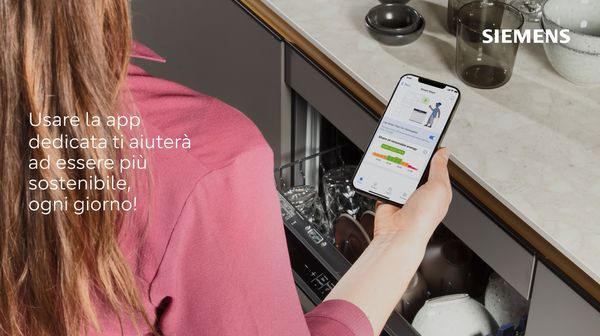 Donna che utilizza l'app per smartphone per controllare la lavastoviglie, promuovere l'uso di elettrodomestici sostenibili.