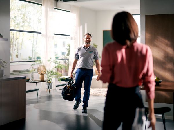 Technician kneels in a modern kitchen to assist with a Siemens home appliance installation. 