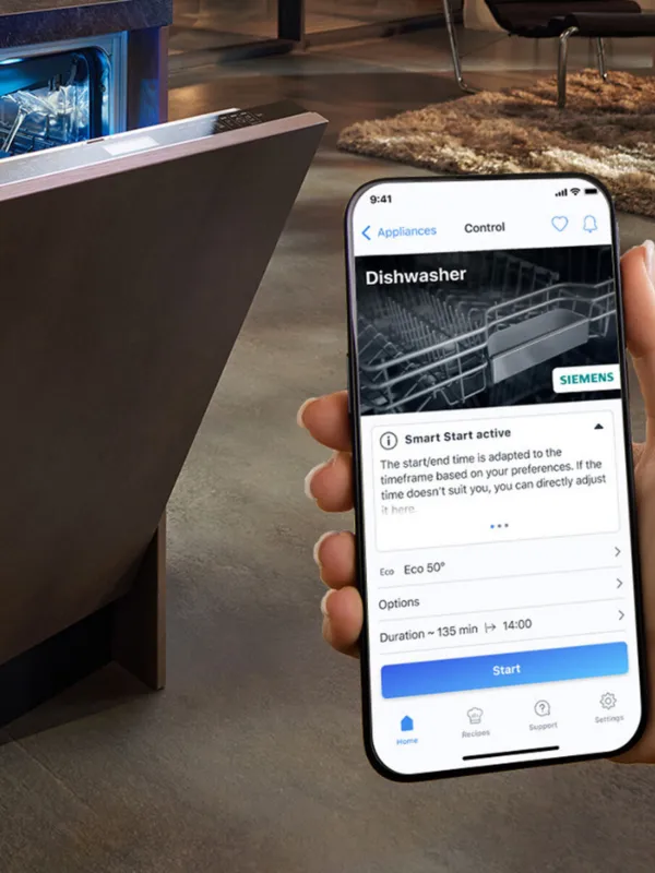 Smartphone displaying dishwasher controls, open dishwasher door in background.