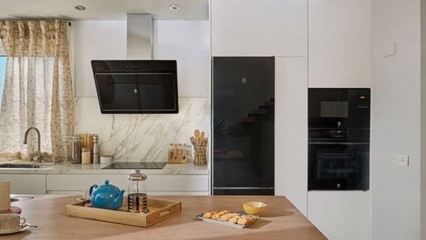 Cocina moderna con elegantes armarios blancos, salpicadero de mármol, electrodomésticos negros y una isla de madera con té y galletas a la vista.