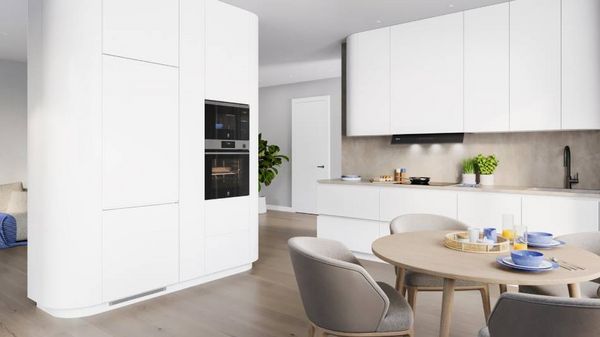 Cocina moderna y elegante con armarios blancos, una mesa redonda de madera para el almuerzo y una pared gris con una planta.