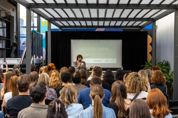 A speaker addresses a crowded audience in a modern venue, with a screen displaying "Western Living" in the background.