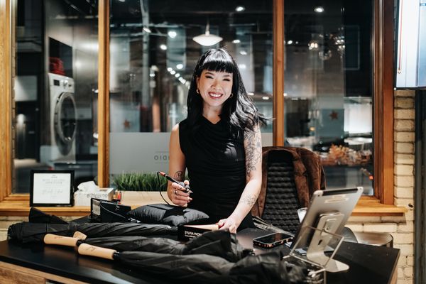 A person in a black outfit stands behind a counter with various items, including umbrellas and a tablet, in a modern, well-lit space.
