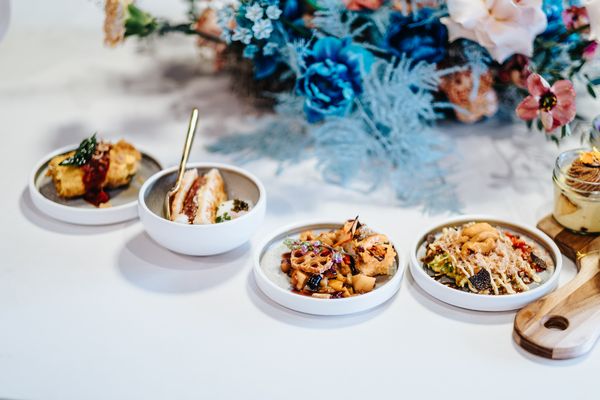 A beautifully arranged platter with four small bowls of gourmet dishes beside a floral centerpiece, showcasing vibrant colors.