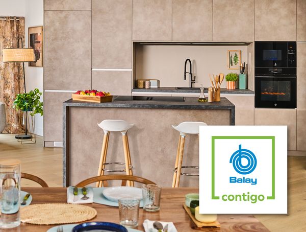 Cocina y sala de estar modernas con un cómodo sofá, una decoración elegante y una elegante isla con frutas, que exhibe electrodomésticos Balay. 