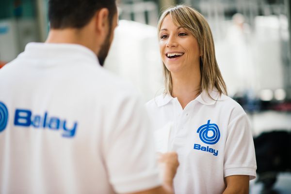 Dos personas con camisas blancas y el logotipo azul de "Balay" están conversando en un entorno interior bien iluminado.   