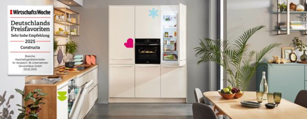 Eine moderne Küche mit einem eleganten weißen Kühlschrank und Backofen, mit lebhaftem Dekor und Pflanzen, die den Constructa-Preis 2025 auszeichnet.