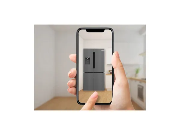 Eine Hand hält ein Smartphone, das einen modernen grauen Kühlschrank in einem hellen