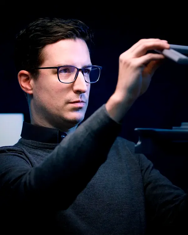 A person in glasses examines a sleek, dark object in a dimly lit environment.