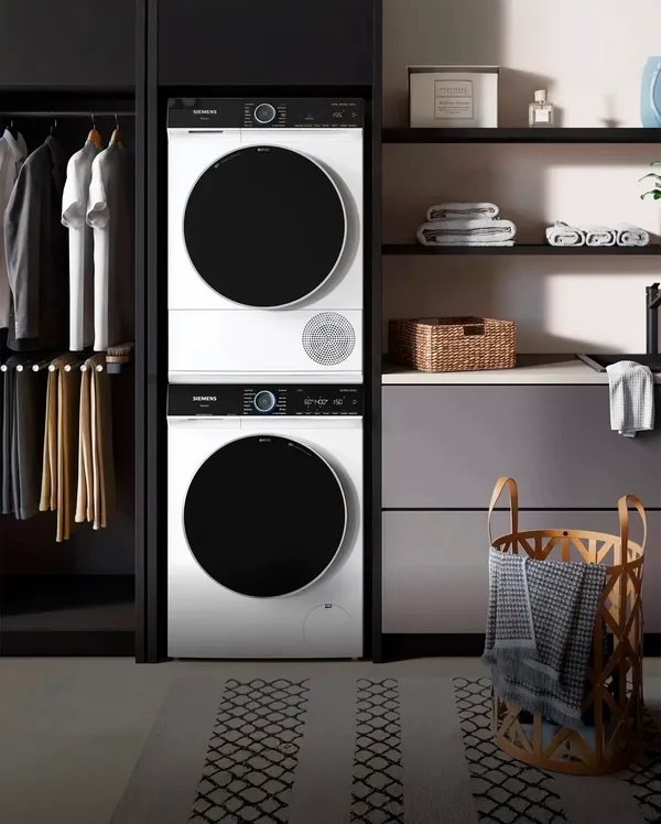 A Siemens laundry space featuring stacked washer and dryer units, surrounded by neatly arranged clothes and storage baskets.