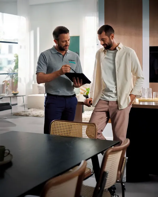 Two men engaged in conversation, one holding a tablet, in a modern, well-lit living space with stylish furniture.