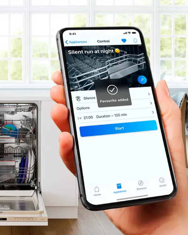 Ruka drži pametan telefon koji prikazuje tiho pranje posuđa u Bosch Home Connect aplikaciji. U pozadini se vidi napunjena mašina za pranje posuđa.