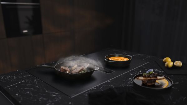 Moderne køkkenbord med grill, gryder til pasta og sovs, friske krydderurter og salat.