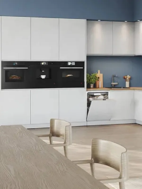 Cucina moderna aperta con una tavolo di legno in primo piano e vari elettrodomestici Bosch da incasso sullo sfondo