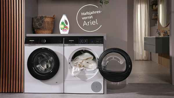 Ariel Flüssigwaschmittel steht auf Siemens Waschmaschine in einer schönen Waschküche und daneben steht der Hinweis auf einen gratis Halbjahresvorrat Waschmittel im Siemens Online Shop