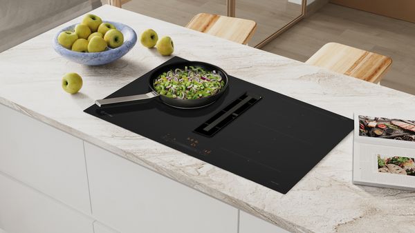 Imagen de placa cristal mate en funcionamiento sobre encimera de cocina, con una sartén con alimentos.