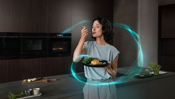 iQ700 Backofen von Siemens. Im Vordergrund steht eine Frau mit einem Teller mit Essen in der Hand.