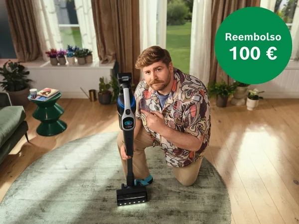 Hombre de rodillas, señalando una aspiradora moderna en el suelo. Un círculo verde indica un reembolso de  100 €.