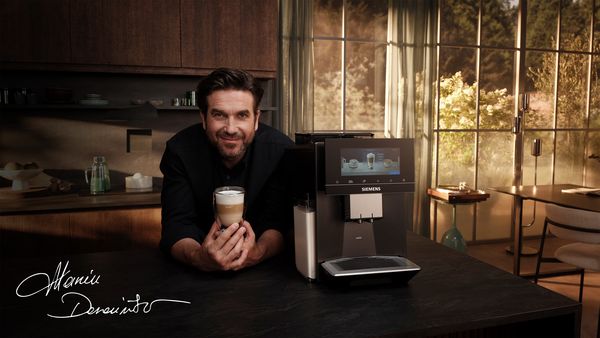 Mężczyzna trzymający filiżankę kawy obok ekspresu do kawy Siemens w eleganckiej  kuchni z dużymi oknami