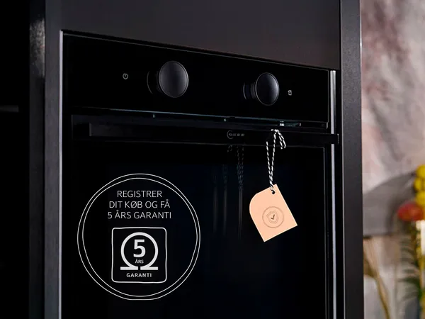 Neff sort indbygget ovn og et hængende mærke på håndtaget, samt et 5-års garantimærke i billedet, i et moderne køkken