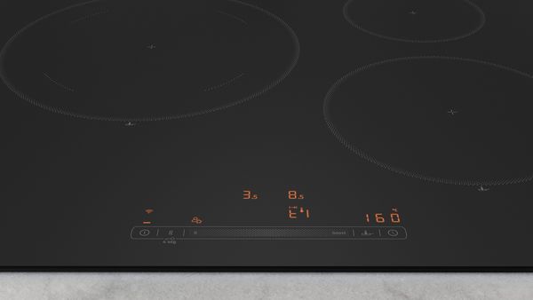 Imagen de placa cristal mate en funcionamiento sobre encimera de cocina, con el control de temperatura visible en el display, con una sartén con alimentos. 