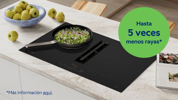 Imagen de placa cristal mate en funcionamiento sobre encimera de cocina, con una sartén con alimentos. 