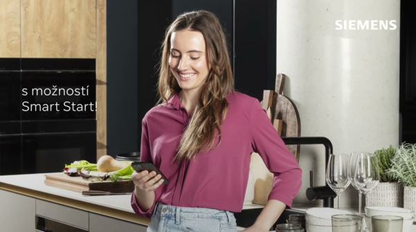 Žena stojí před myčkou Siemens a dívá se na funkci smartStart na smartphonu.