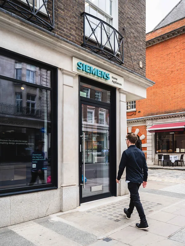 A man walks past the exterior of a Siemens Home Appliances showroom with large glass windows and a prominent Siemens sign.