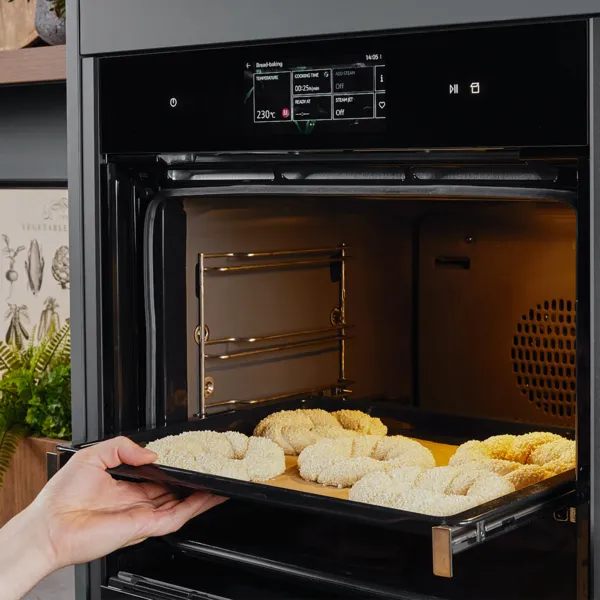Eine Hand schiebt den zu Simits geformten Teig auf einem Backblech in den Backofen.