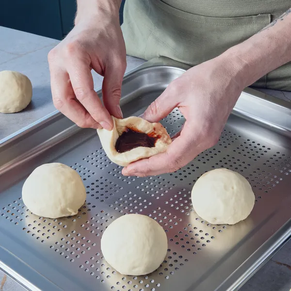 Eine Person füllt Teig mit Pflaumenmuss, um Klöße zu formen, und legt die Klöße auf ein gelochtes Blech, um sie zu dämpfen.