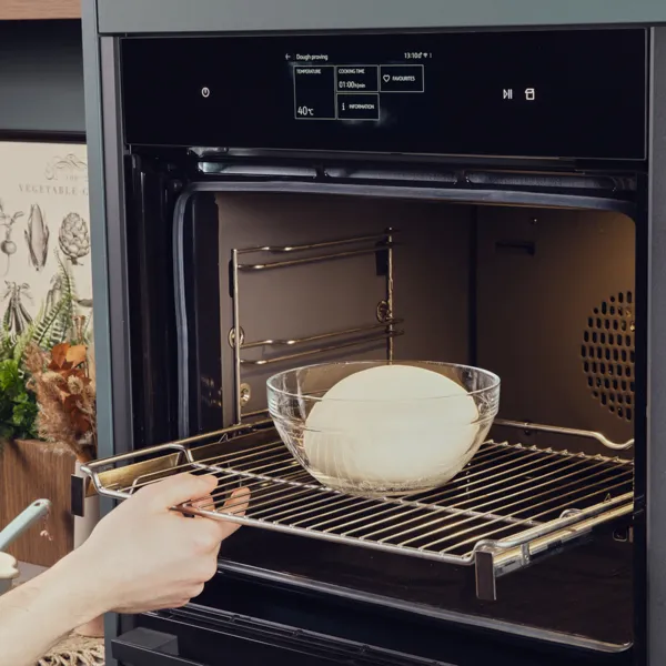 Eine Glasschüssel mit einer Teigkugel wird in den Backofen geschoben.