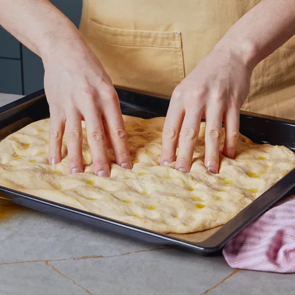 Due mani premono dei buchi in un impasto steso e coperto d'olio.