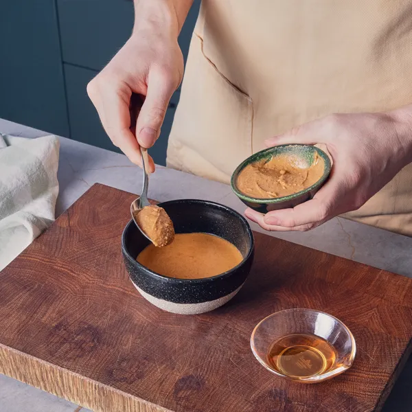 Una mano aggiunge un cucchiaio di burro d'arachidi a una ciotola piena a metà.