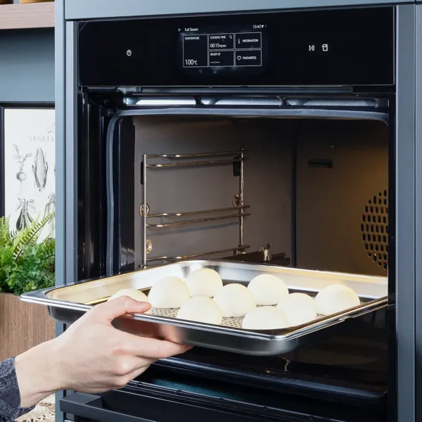 Eine Person schiebt ein Blech mit vorbereiteten Teigtaschen mit Schweinefleischfüllung zum Garen in einen Dampfbackofen.