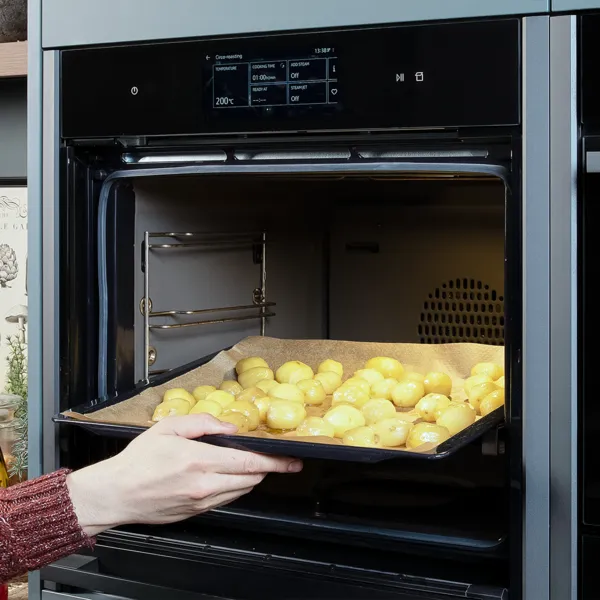 Ein Backblech mit geschälten Kartoffeln wird in einen geöffneten Backofen geschoben.