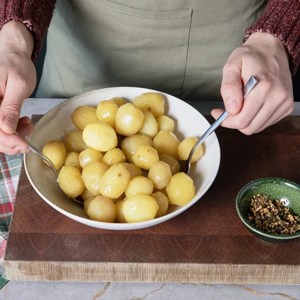 Geschälte Kartoffeln werden in einer großen Schüssel mit Öl, Rosmarin und Knoblauch geschwenkt.