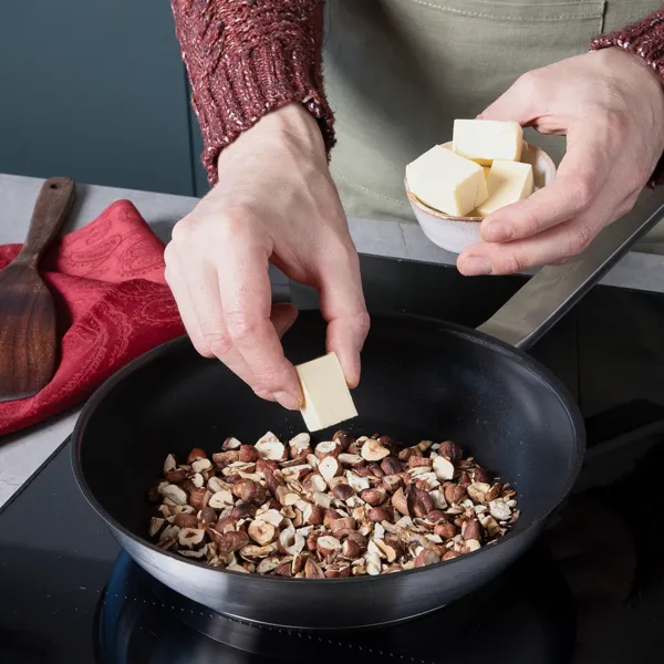 Haselnüsse rösten in einer Pfanne auf dem Kochfeld, während Butter hinzugegeben wird.
