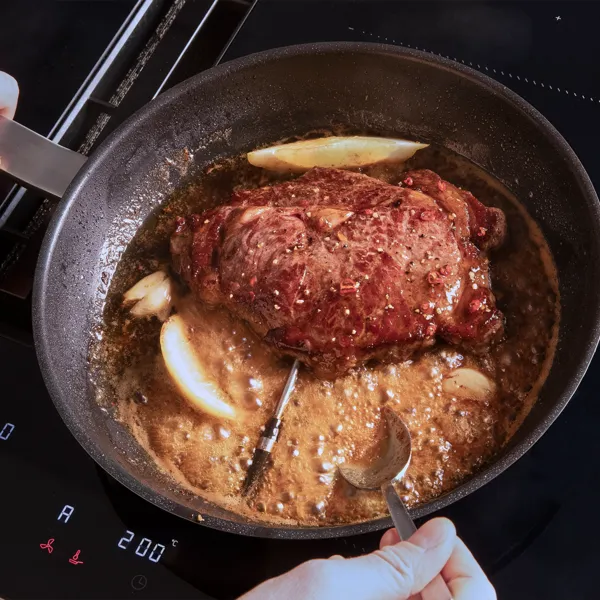 Ein Steak wird in einer schwarzen Pfanne zusammen mit einer Sauce und Zitronenspalten gegrillt.