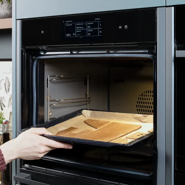 Zugeschnittene Lebkuchenteile auf einem Backblech werden in einen geöffneten Backofen geschoben.