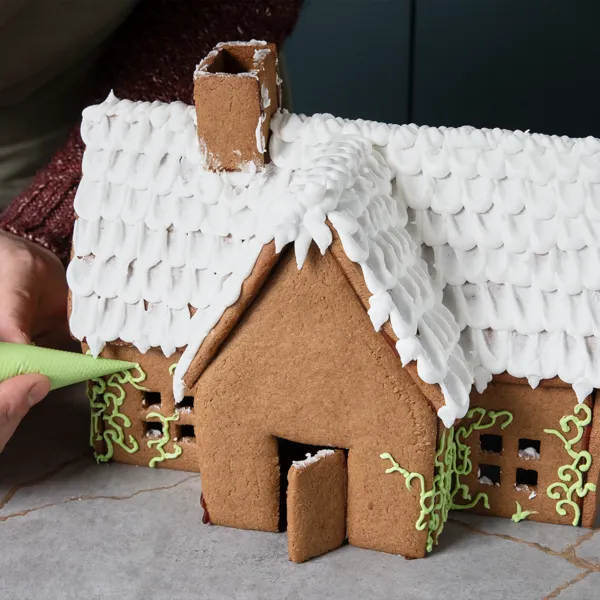Zuckerguss wird als Dekoration auf ein fertiges Lebkuchenhaus gespritzt.