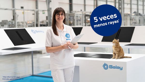 Empleada de Balay en zona ficticia de pruebas mirando sonriente a c&aacute;mara junto a una encimera ** con una placa mate y un gato naranja, con un bolo con el mensaje 5 veces menos rayas.