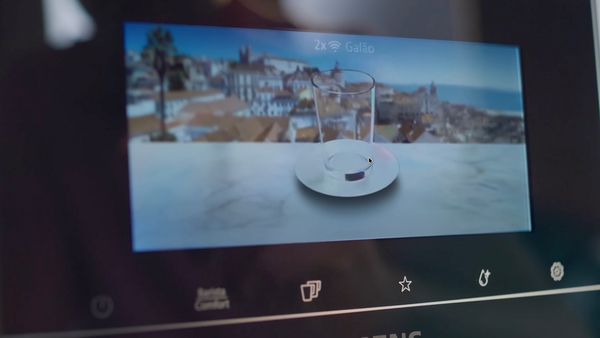 Dwie osoby piją kawę przy drewnianym stole, duży ceramiczny kogut jako dekoracja.   