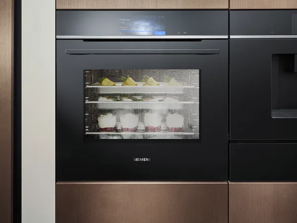 Ein moderner Siemens Dampfbackofen mit klarer Glastür, der dampfende Gerichte auf mehreren Einschüben zeigt.